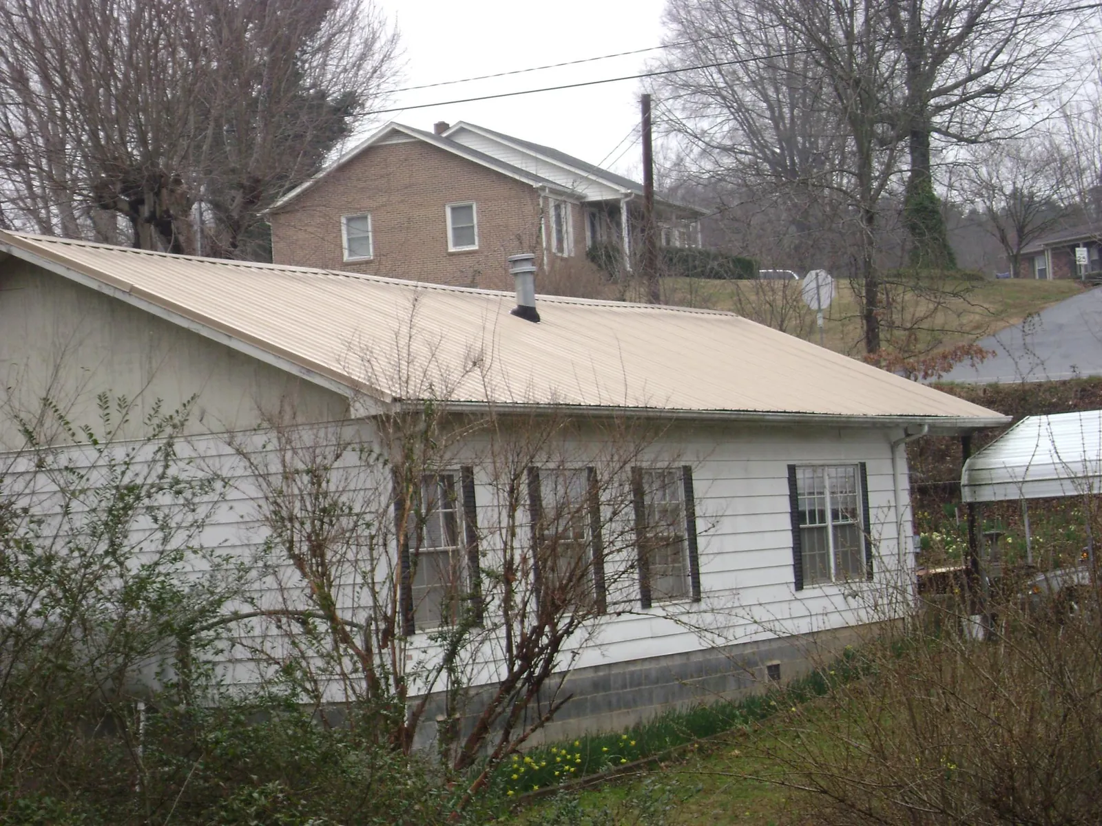 Tan metal roof on a white sided house set into a hillside — Commercial Roofing by Roofing Brothers in Hopedale
